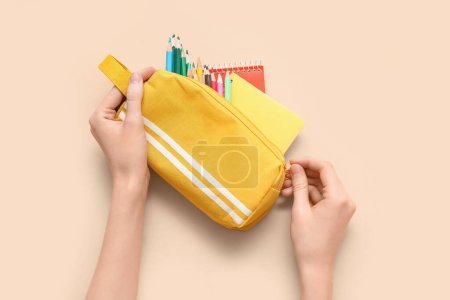 Foto de Manos de niño con estuche de lápiz, diferentes artículos de papelería escolar y cuadernos sobre fondo beige - Imagen libre de derechos