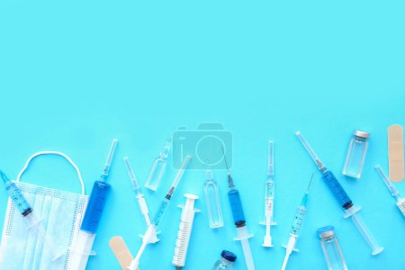 Medizinische Spritzen mit Medikamenten, Ampullen und Maske auf blauem Hintergrund