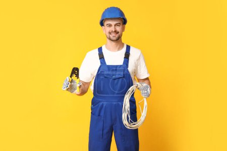 Foto de Retrato de electricista masculino con rizador y alambres sobre fondo amarillo - Imagen libre de derechos