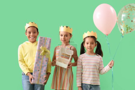 Photo for Cute little children in crowns with Birthday gift, cake and balloons on green background - Royalty Free Image