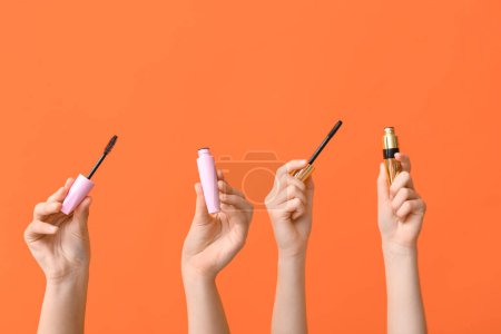 Weibliche Hände mit Mascaras auf orangefarbenem Hintergrund