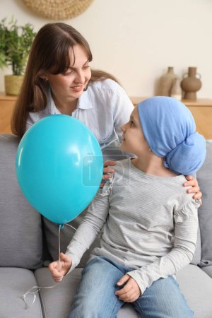 Téléchargez les photos : Petite fille après chimiothérapie avec ballon bleu et sa mère à la maison. Journée internationale du cancer chez les enfants - en image libre de droit