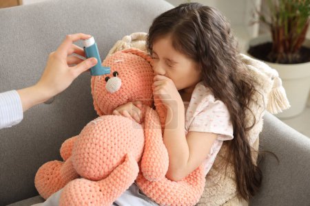 Téléchargez les photos : Petite fille ayant une crise d'asthme et sa mère avec inhalateur à la maison - en image libre de droit