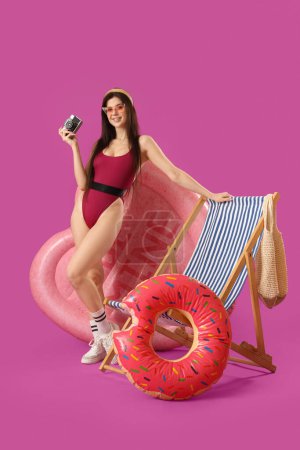 Téléchargez les photos : Portrait de jolie jeune femme avec anneau gonflable, matelas et transat sur fond rose - en image libre de droit