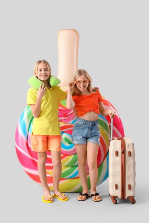 Téléchargez les photos : Petits enfants mignons avec matelas gonflable en forme de bonbons et valise sur fond gris - en image libre de droit
