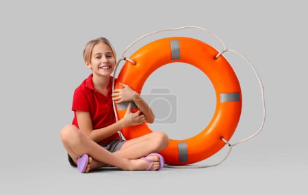 Photo for Happy little boy lifeguard with ring buoy sitting on grey background - Royalty Free Image