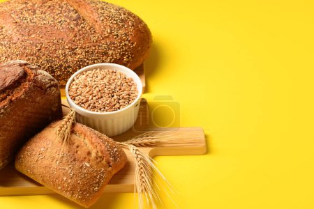 Photo for Wooden board with loaves of fresh bread, wheat spikelets and grains on yellow background - Royalty Free Image