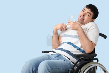 Young man with glass of water in wheelchair on blue background. National Cerebral Palsy Awareness Month