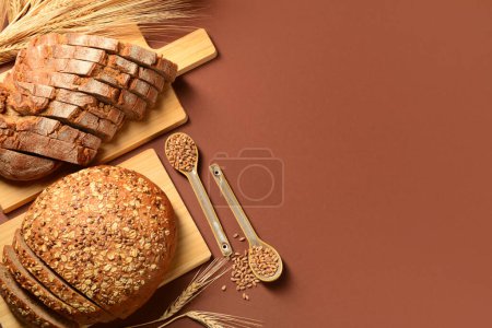 Photo for Wooden boards with sliced loaves of bread, wheat spikelets and grains on brown background - Royalty Free Image