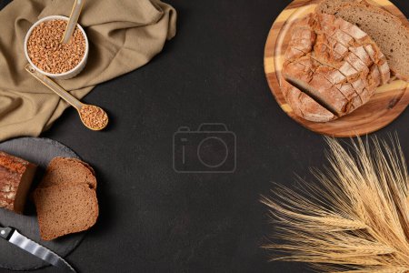 Photo for Boards with sliced loaves of bread, wheat spikelets and grains on black background - Royalty Free Image