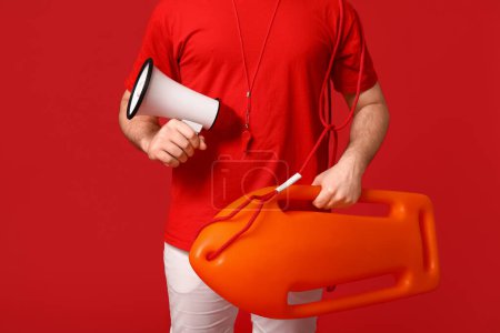 Sauveteur mâle avec bouée de sauvetage et mégaphone sur fond rouge
