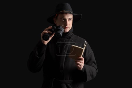 Téléchargez les photos : Homme espion avec jumelles et carnet sur fond noir - en image libre de droit