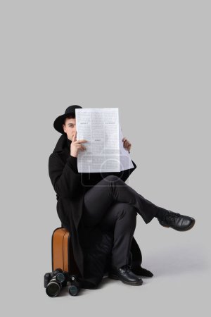 Téléchargez les photos : Homme espion avec journal assis sur sac sur fond clair - en image libre de droit