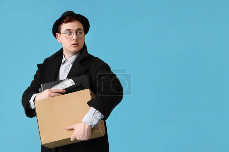 Foto de Espía masculino con pistola en caja sobre fondo azul - Imagen libre de derechos