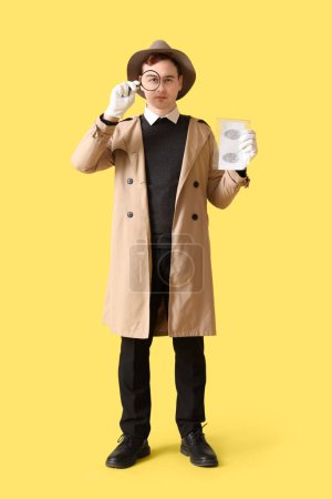 Téléchargez les photos : Homme espion avec loupe et empreintes digitales sur fond jaune - en image libre de droit