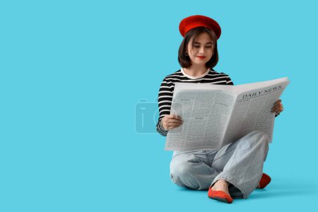 Portrait of fashionable young woman in beret reading newspaper on blue background