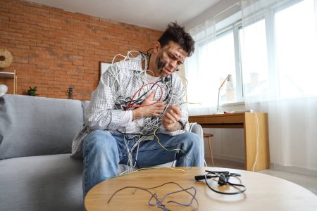 Hombre joven electrocutado con la cara quemada y cables sentados en el sofá en casa