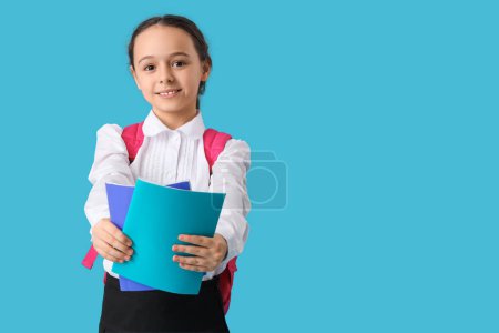 Photo for Happy little schoolgirl with backpack and notebooks on blue background - Royalty Free Image