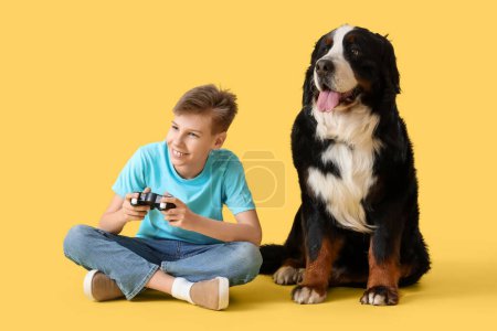 Kleiner Junge mit Berner Sennenhund beim Videospiel auf gelbem Hintergrund