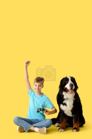 Little boy with Bernese mountain dog playing video game on yellow background