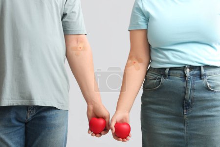 Blood donors with applied medical patches and hearts on grey background, closeup