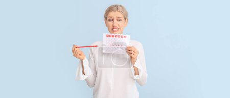 Photo for Stressed young woman with menstrual calendar on light blue background - Royalty Free Image