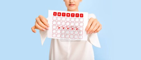 Photo for Young woman with menstrual calendar on light blue background, closeup - Royalty Free Image