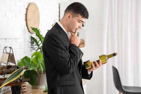 Photo for Thoughtful young sommelier with bottle of wine in kitchen - Royalty Free Image