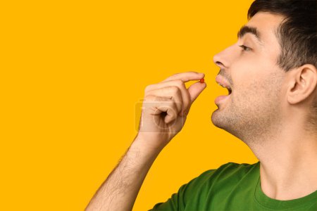 Photo for Young man taking vitamin A pill on yellow background, closeup - Royalty Free Image