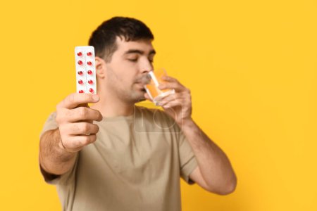 Foto de Hombre joven con ampolla de píldoras de vitamina A beber agua sobre fondo amarillo, primer plano - Imagen libre de derechos