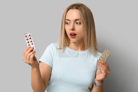 Young woman with blisters of vitamin A pills on light background