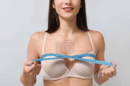 Téléchargez les photos : Jeune femme mesurant sa poitrine sur fond gris - en image libre de droit