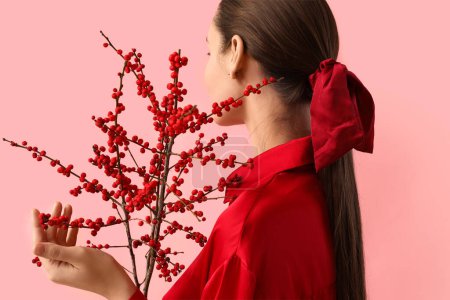 Beautiful young woman with ponytail and scrunchy holding berry branches on pink background