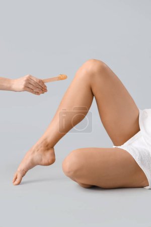 Photo for Legs of beautiful young woman and hand holding spatula with sugaring paste on grey background - Royalty Free Image