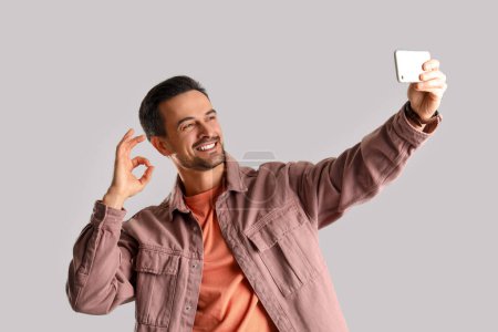 Foto de Hombre guapo mostrando OK y tomando selfie sobre fondo claro - Imagen libre de derechos