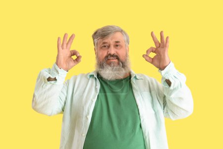 Téléchargez les photos : Mature barbu homme montrant OK sur fond jaune - en image libre de droit