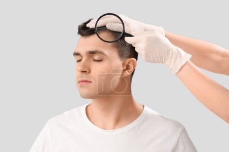 Photo for Doctor with magnifier examining young man's hair on light background, closeup - Royalty Free Image
