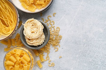 Photo for Different uncooked pasta in bowls on light background - Royalty Free Image
