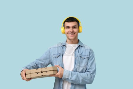 Photo for Young man holding cardboard boxes with tasty pizzas on blue background - Royalty Free Image