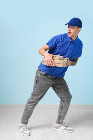 Photo for Delivery man holding cardboard boxes with tasty pizzas near blue wall - Royalty Free Image