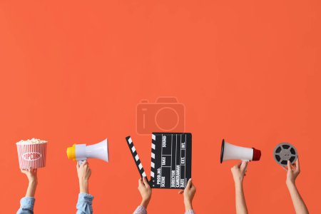 Téléchargez les photos : Beaucoup de mains avec seau de pop-corn, film clapper et mégaphones sur fond orange - en image libre de droit