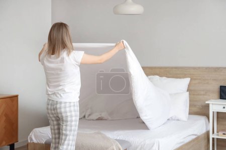 Photo for Young woman making bed in bedroom, back view - Royalty Free Image