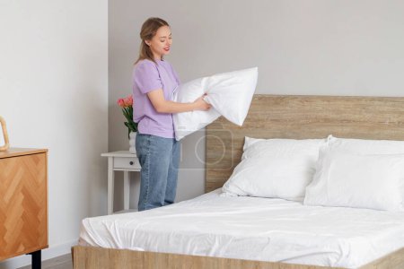 Photo for Pretty young woman putting pillow on bed in bedroom - Royalty Free Image