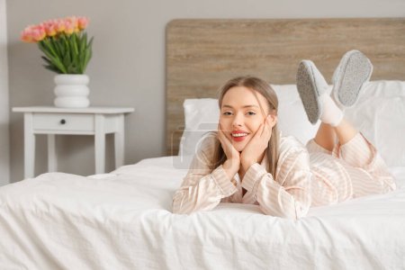 Photo for Pretty young woman in pajamas lying on comfortable bed in light bedroom - Royalty Free Image