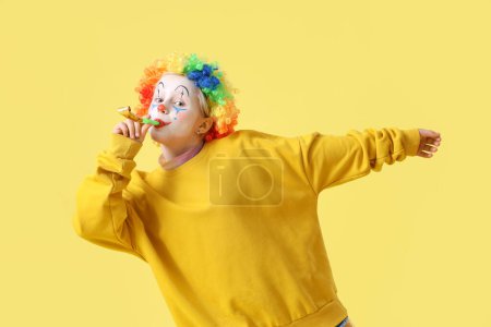 Foto de Muchacha divertida en peluca de payaso con ventilador de fiesta sobre fondo amarillo. Celebración del Día de los Inocentes - Imagen libre de derechos