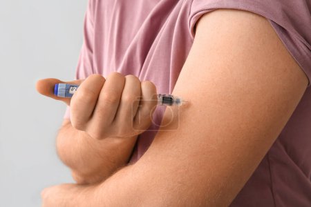 Handsome young diabetic man giving himself insulin injection on grey background, closeup