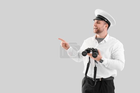Photo for Young male sailor with binoculars pointing at something on white background - Royalty Free Image