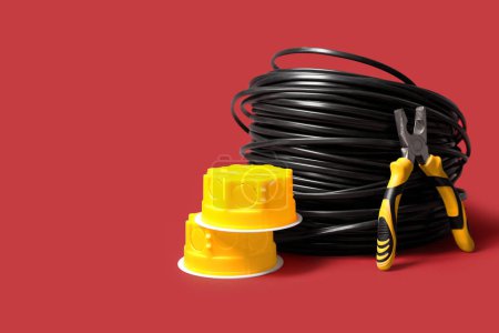Elektrische Anschlussdosen, Zangen und Kabel auf rotem Hintergrund