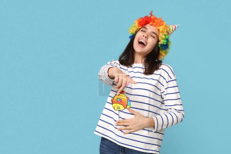 Foto de Hermosa joven feliz mujer en disfraz divertido con peces de papel riendo sobre fondo azul. Celebración del día del tonto de abril - Imagen libre de derechos