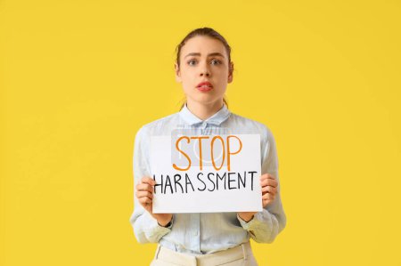 Téléchargez les photos : Jeune femme d'affaires tenant du papier avec texte STOP HARASSMENT sur fond jaune - en image libre de droit